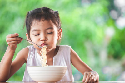 Cute girl eating noodles at table in public park