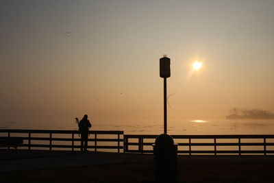 Silhouette man by sea against sky during sunset