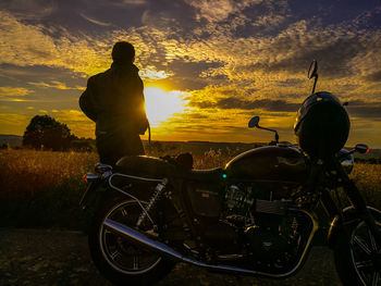 Man with motorcycle against sky during sunset
