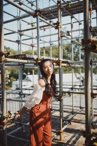 Portrait of beautiful woman standing by metallic built structure