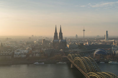 Bridge over river in city against sky during sunset