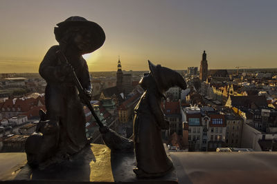 Statue against buildings in city at sunset