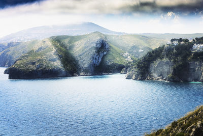 Scenic view of sea by mountain against sky