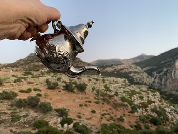 Close-up of hand holding metal against sky