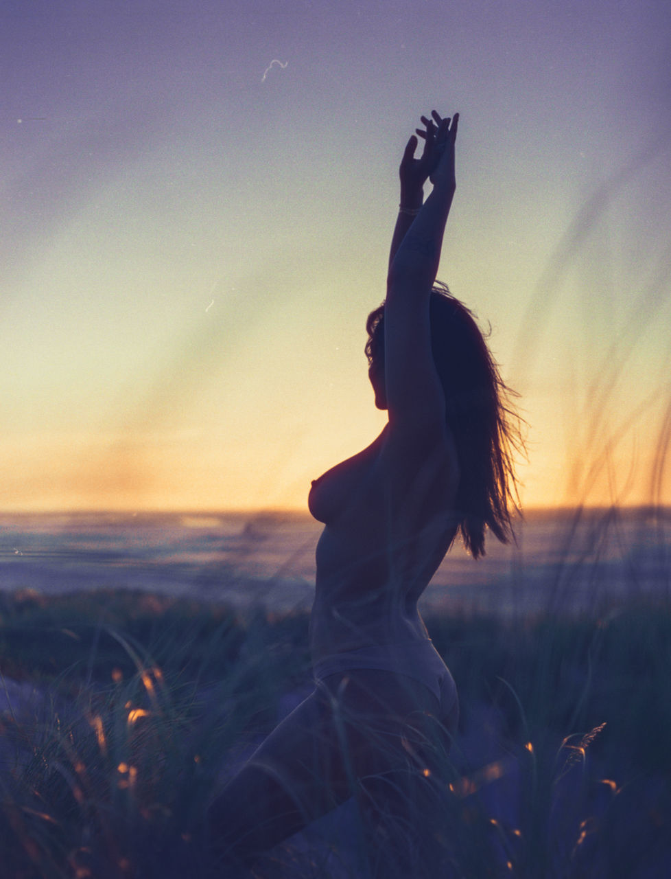 sunset, sky, one person, land, lifestyles, real people, women, leisure activity, arms raised, nature, human arm, beauty in nature, adult, water, silhouette, sea, orange color, outdoors, beach, hairstyle