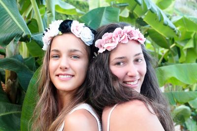 Portrait of smiling friends wearing flowers by plants