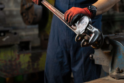 Midsection of worker adjusting equipment with wrench in workshop