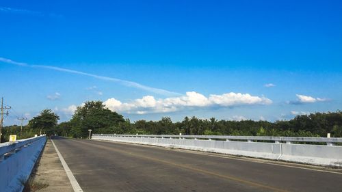 Road by trees against blue sky