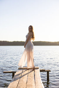 Beautiful girl in a white dress, walking along a wooden pier on the bank of a river or a lake