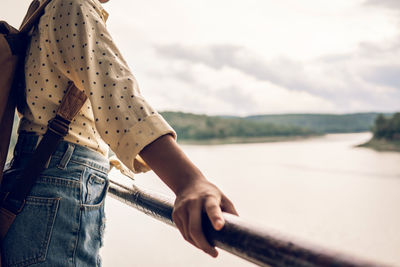 Midsection of woman standing by railing against sky