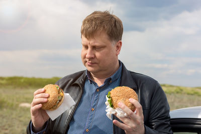 Hungry man in fresh air makes a choice between two burgers.