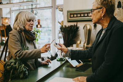 Senior female customer talking to owner while doing online payment at store