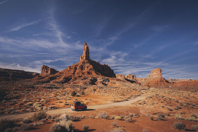 An orange car is driving through the valley of gods, utah