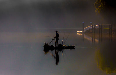 Silhouette people on boat in lake against sky