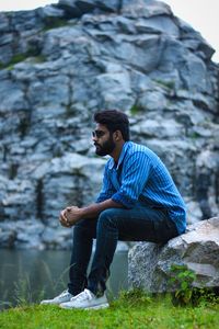 Side view of young man looking away while sitting on rock