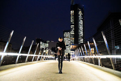 Full length portrait of woman standing on illuminated footbridge in city at night