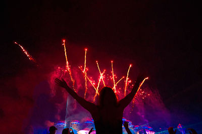 Silhouette woman with arms raised enjoying firework display at night