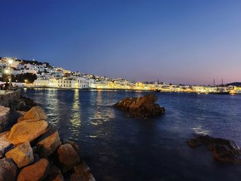 Sea by illuminated city against sky at dusk