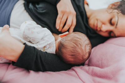 Close-up of mother breastfeeding new born on bed at home