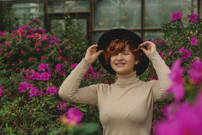 A beautiful plus size girl in a hat smiles among the green plants of greenhouse