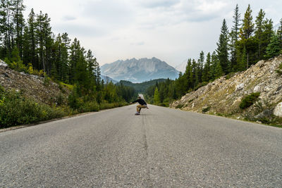 Rear view of young man skateboarding on country road against sky