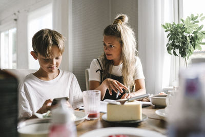 Mother teaching while son using smart phone at home