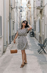 Portrait of attractive young woman standing in alley. summer dress, style, lifestyle.