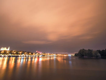 Illuminated city by sea against sky at night