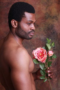 Shirtless young man holding flower while standing against wall