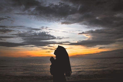 Silhouette woman standing on beach against sky during sunset