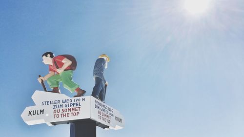 Low angle view of sign board and sculptures against sky