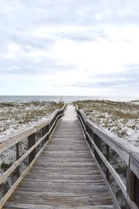 Wooden footbridge leading towards sea against sky