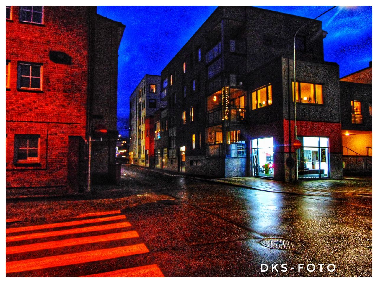 ILLUMINATED STREET BY BUILDINGS AGAINST SKY AT NIGHT