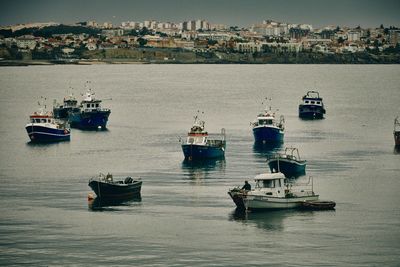 Fishing boats in sea against buildings in city