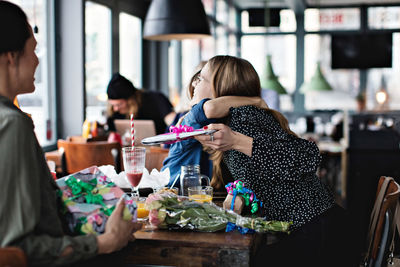 Young woman looking at female friends embracing while sitting at restaurant