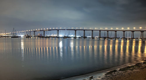 Illuminated bridge over sea against sky at night