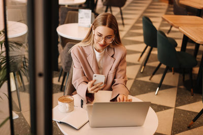 A millennial business woman with glasses works and studies online using mobile phone and technology 