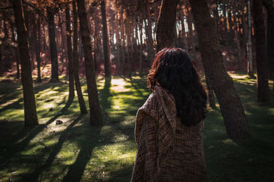 Woman standing by tree trunk in forest