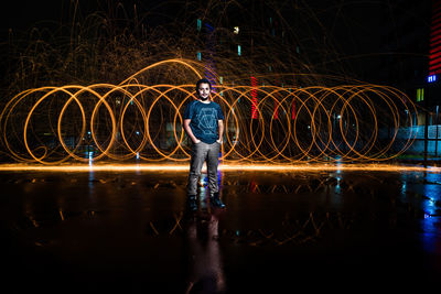 Portrait of young man standing against wire wool at night