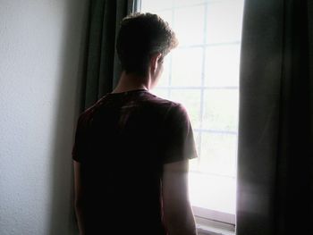 Rear view of teen boy looking through window