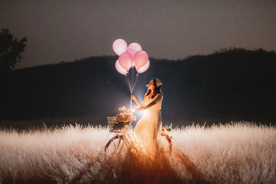 Young woman holding balloons on field against sky