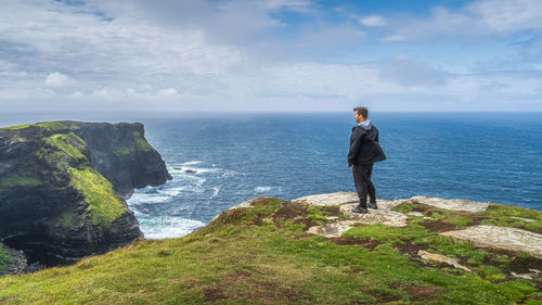 Rear view of man standing on rock by sea against sky