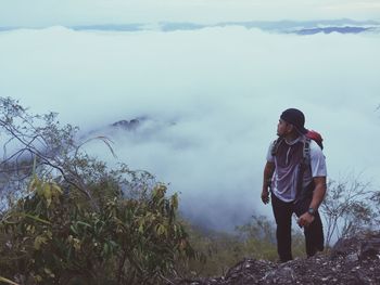 High angle view of male hiker standing on mountain against cloudscape