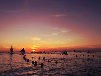 People enjoying in sea against sky during sunset