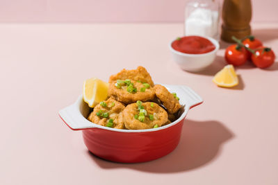 Crispy nuggets in a plate and ketchup on a pink background with hard shadows.