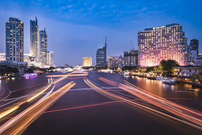Light trails on road amidst buildings against sky at dusk