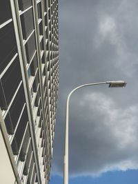 Low angle view of street light by building against cloudy sky