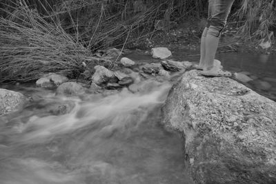 Low section of person standing on rock by stream