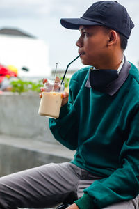Man holding drink sitting in front of hat