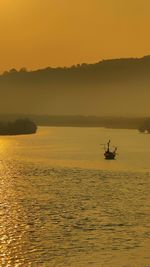 Silhouette boat sailing in sea against orange sky